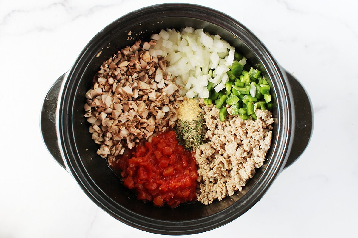 Chopped vegetables, browned ground meat and seasonings in a black pot.