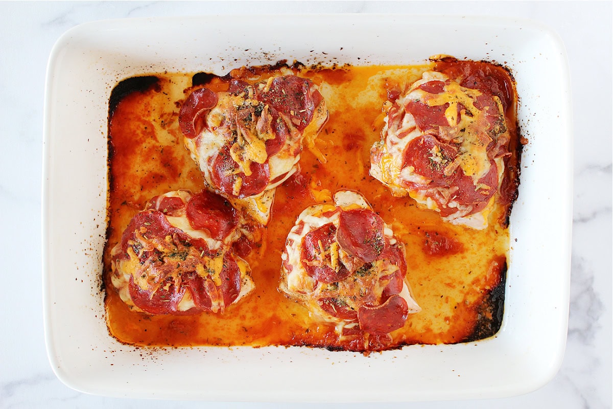 Four baked chicken breasts with melted cheese and turkey pepperoni in a baking dish.