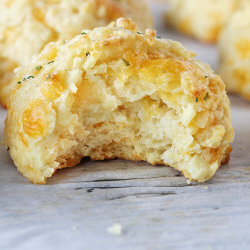 A bite taken out of a garlic cheddar biscuit on a sheet pan.