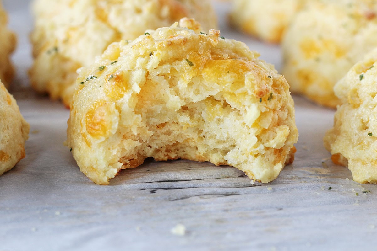 A bite taken out of a garlic cheddar biscuit on a sheet pan.