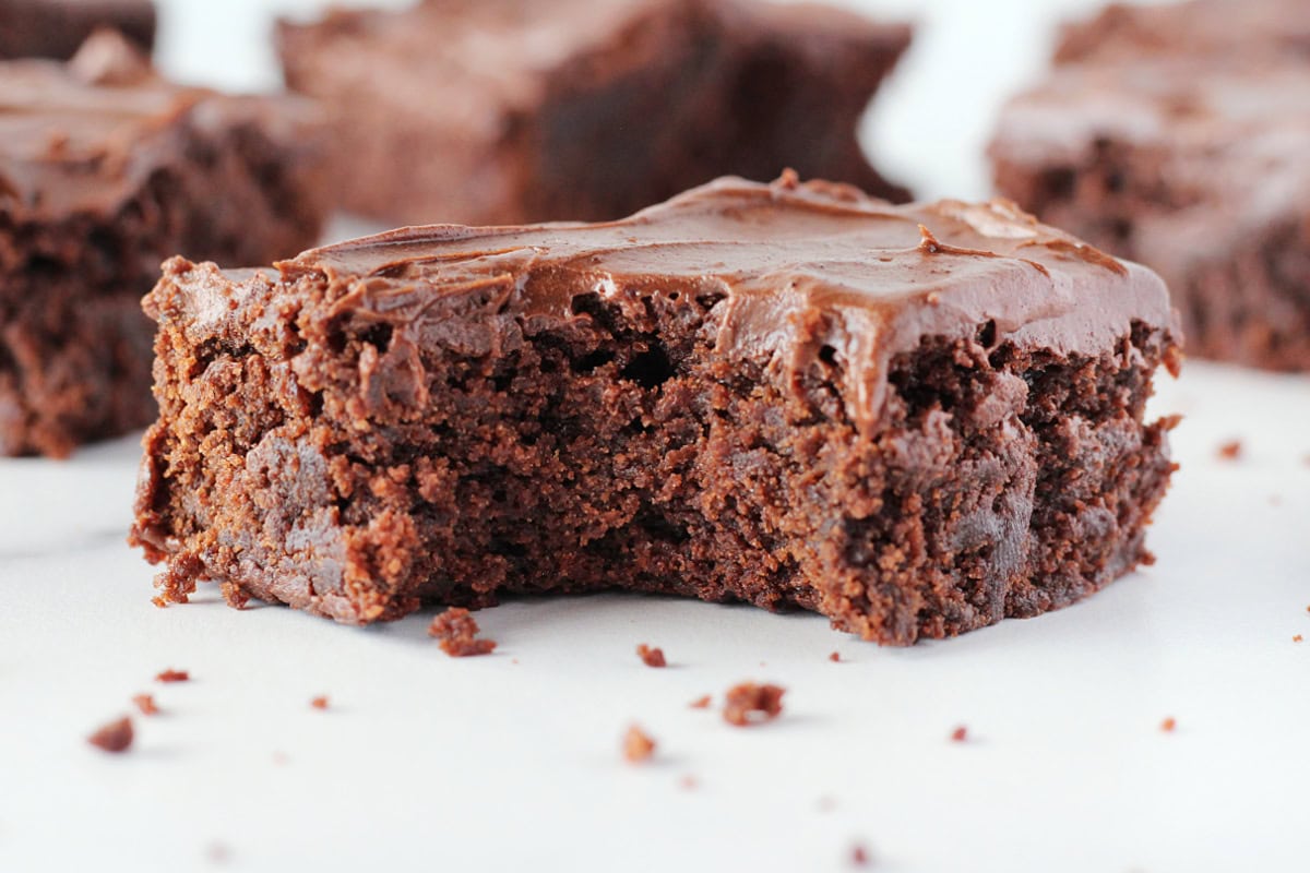 A bite taken out of a chocolate brownie with chocolate frosting on top.