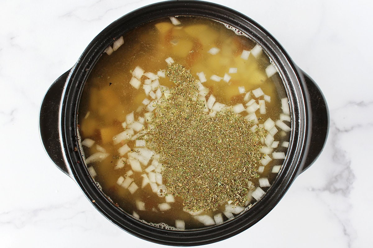 Italian seasoning on top of broth and diced onions in a soup pot.