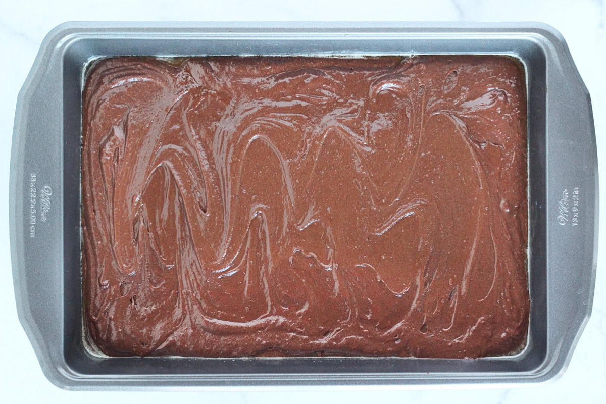 Brownie batter in a metal 9x13 pan.