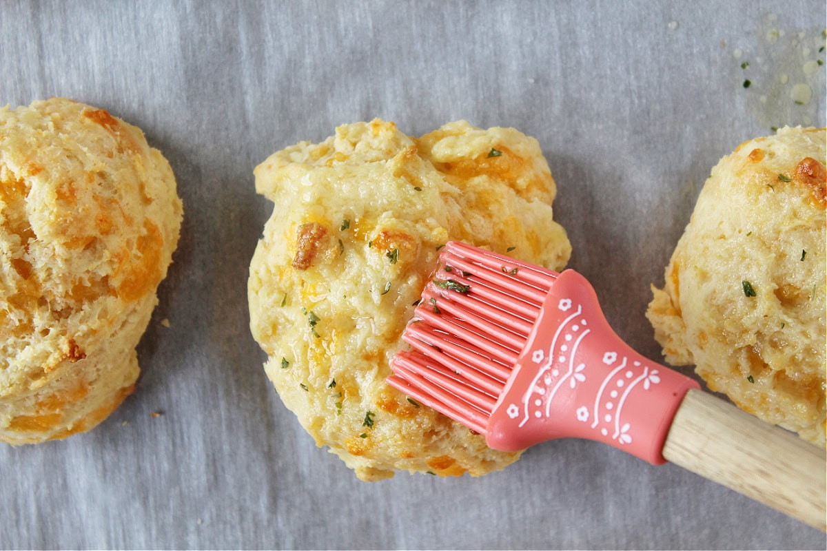 Brushing garlic butter with parsley on a hot cheddar biscuit.