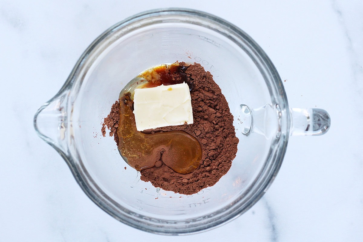 Butter, honey, vanilla extract and cocoa powder in a glass mixing bowl.