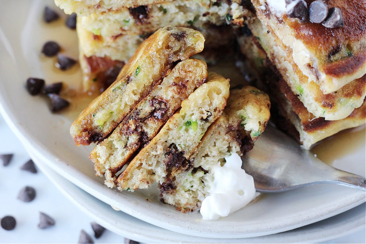 Four zucchini pancakes with chocolate chips and whipped cream on a fork.
