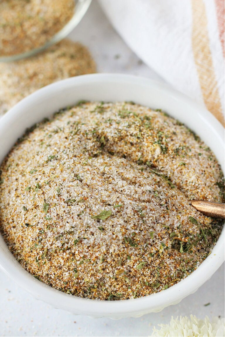 A burger seasoning blend in a white bowl with a copper spoon.