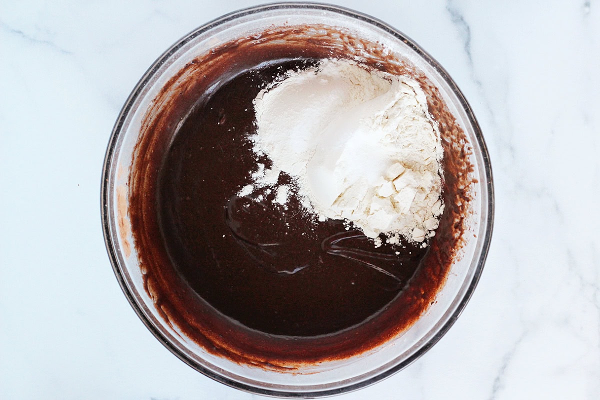 Wet ingredients in a glass mixing bowl with flour on top.