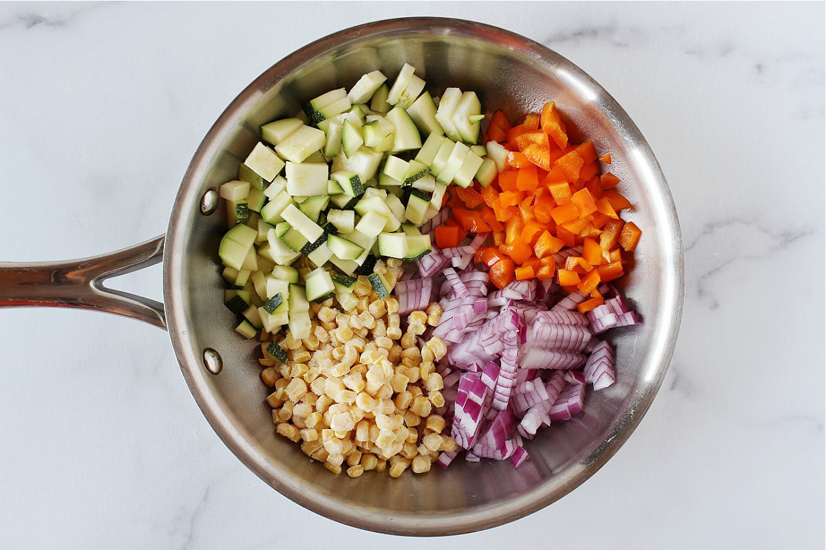 Diced veggies and frozen corn in a stainless steel sauté pan.