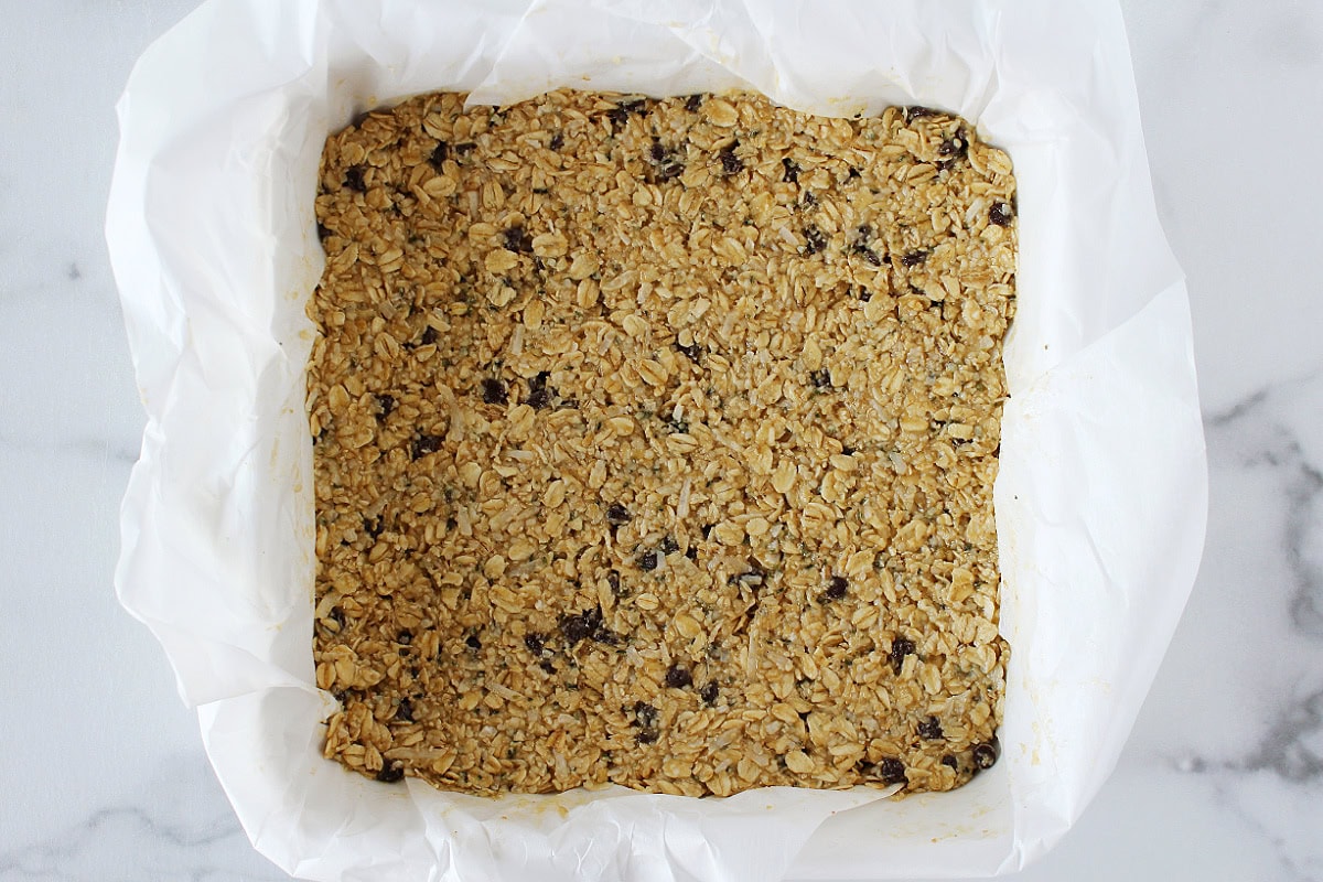 Granola bar batter pressed into a parchment paper lined 8x8 pan.