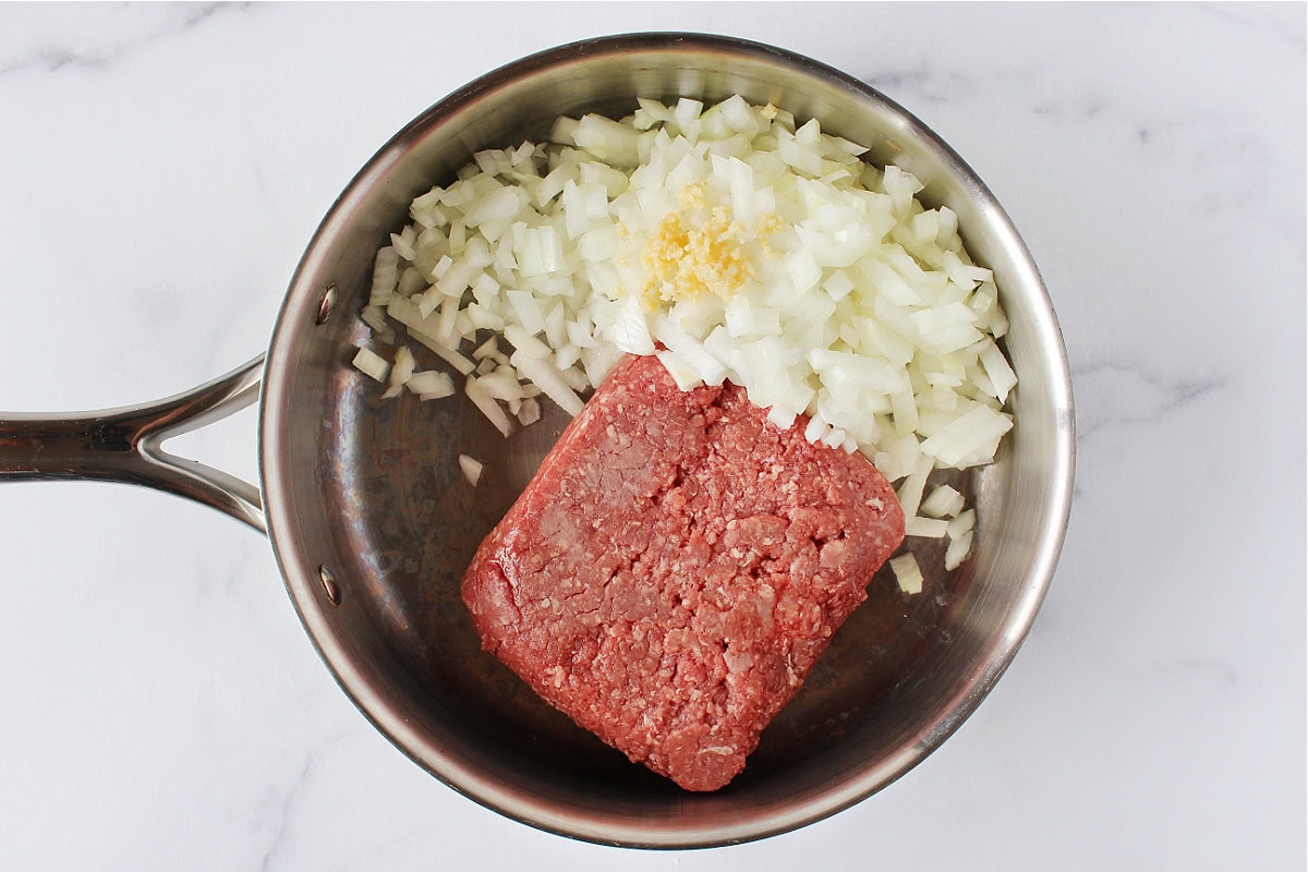 Diced onion, minced garlic and raw ground beef in a stainless steel sauté pan.