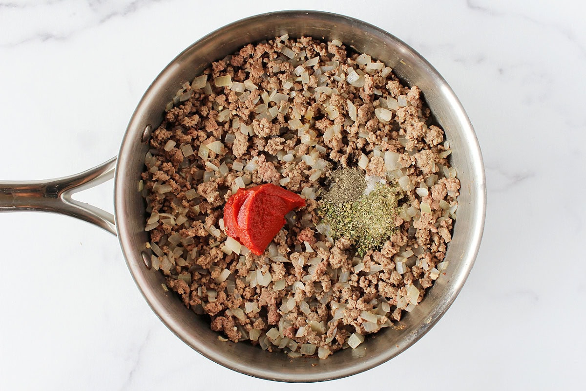 Tomato paste and seasonings on top of browned ground beef and onions.
