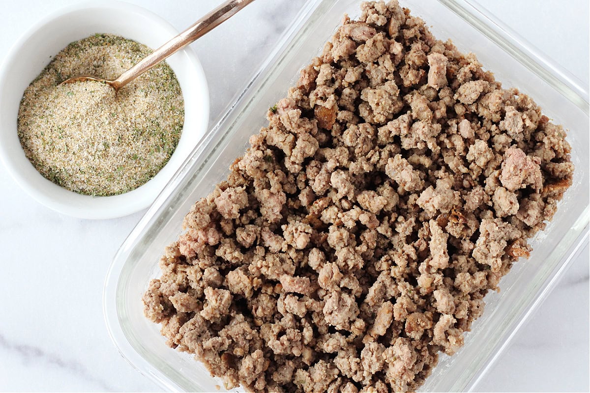 Browned ground beef in a glass container next to a burger seasoning blend.