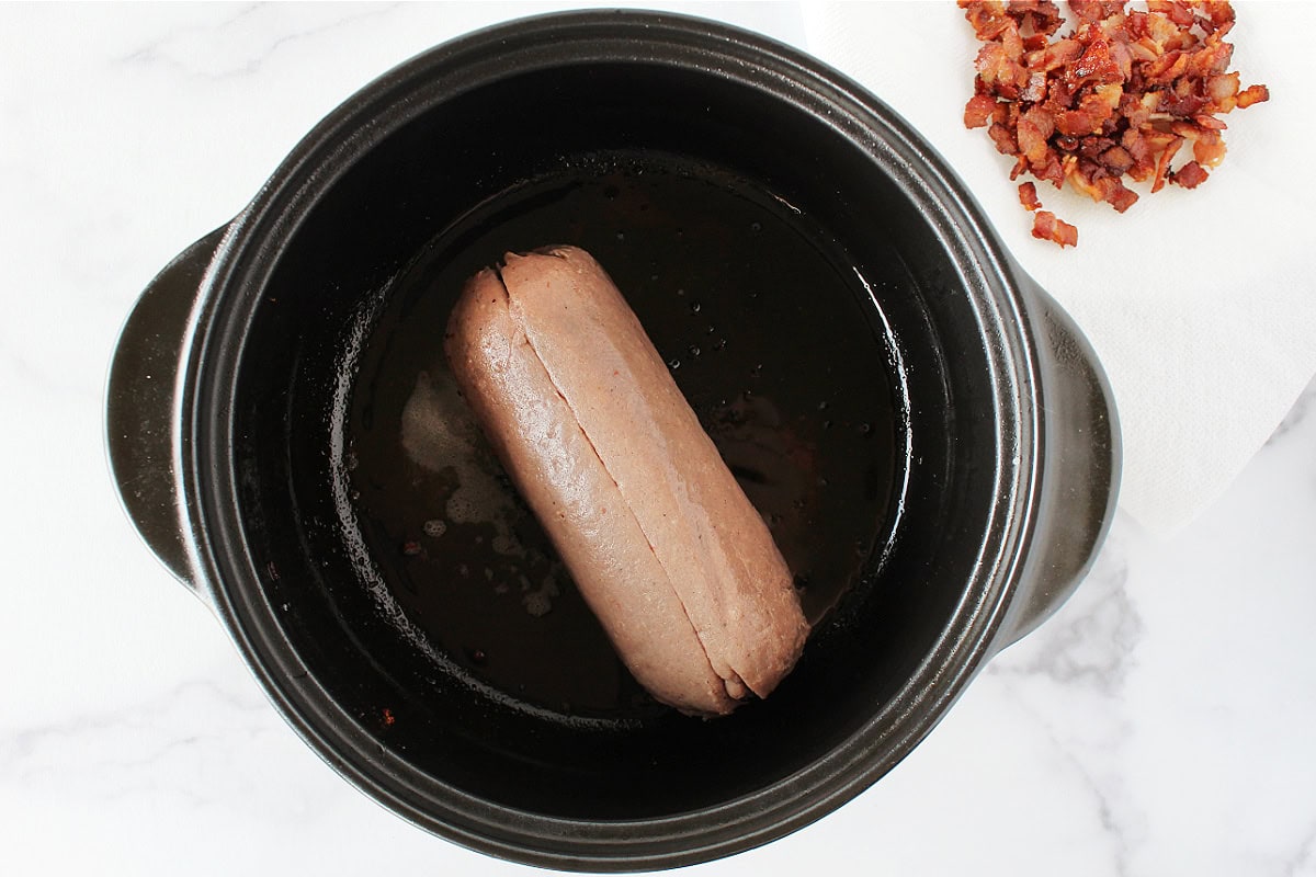 Turkey sausage in a black soup pot with crumbled bacon on the side.