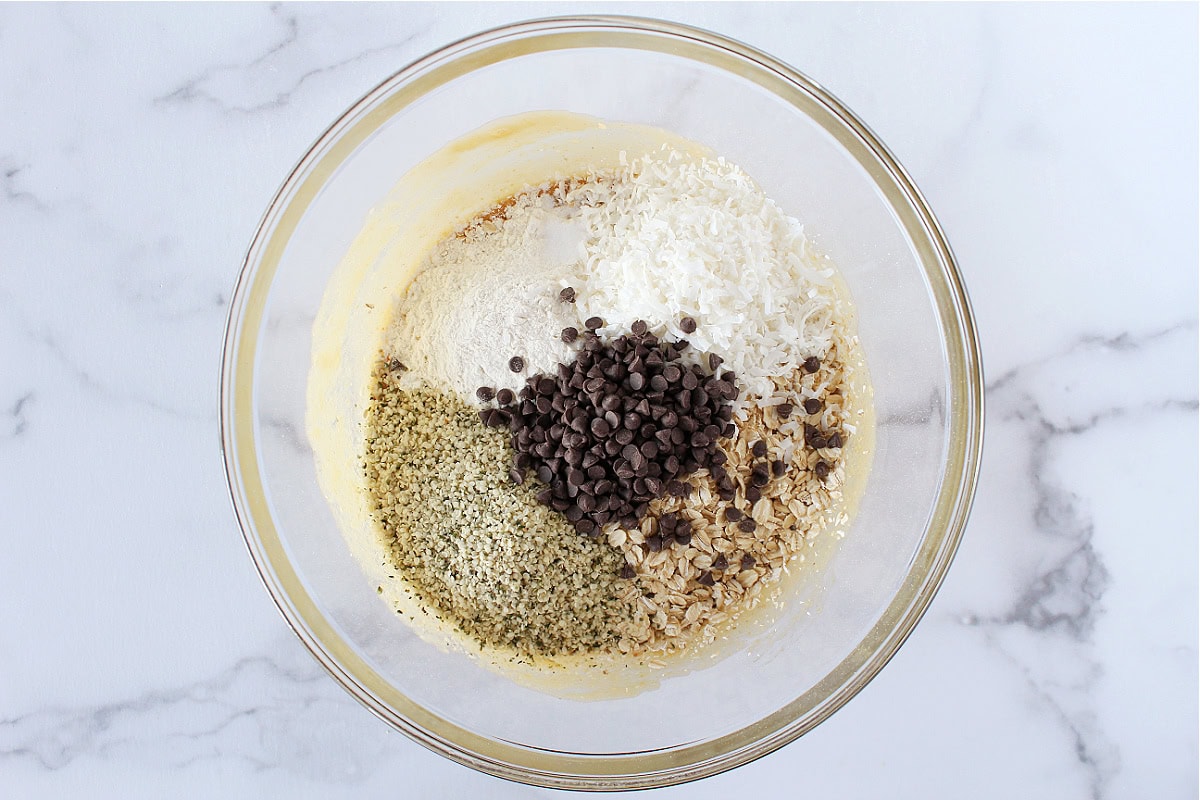 Mini chocolate chips, hemp hearts, oats, and shredded coconut in a glass bowl.