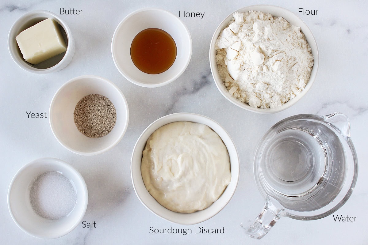 Labeled ingredients for discard sourdough loaf on a white marble countertop.