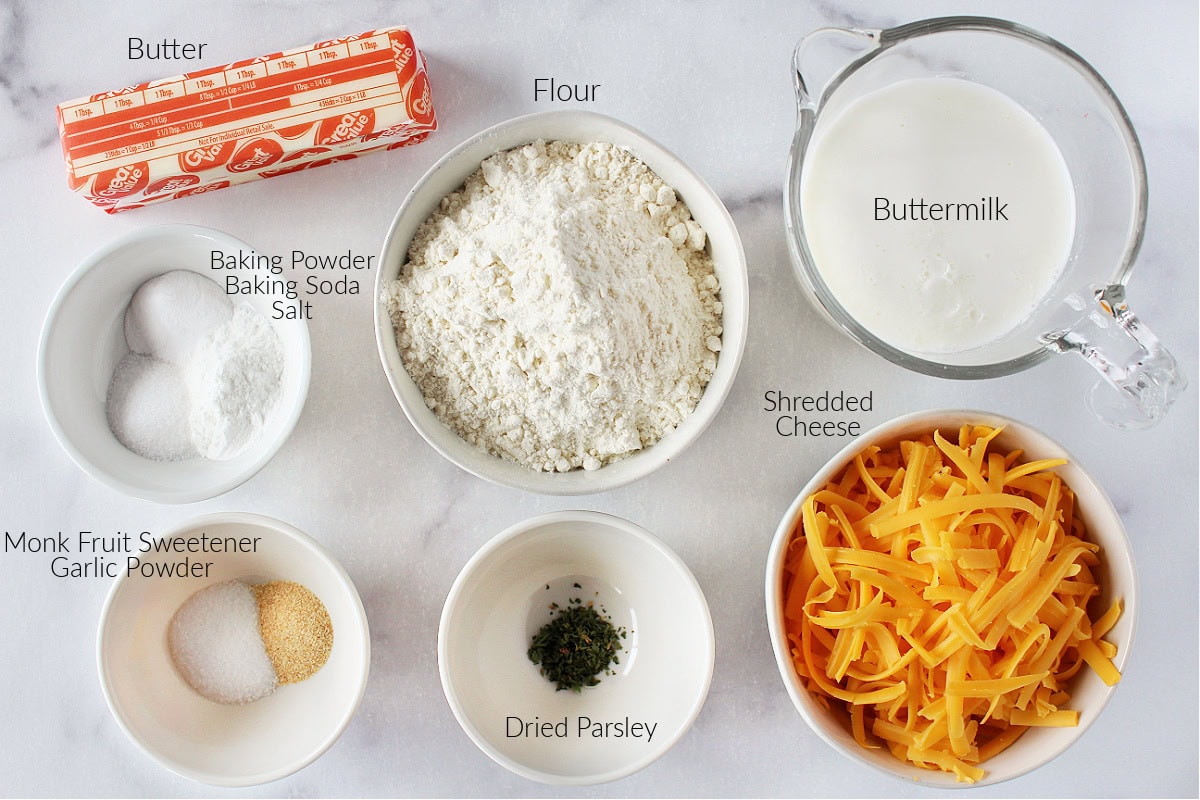 Labeled ingredients for garlic cheddar biscuits on a white marble countertop.