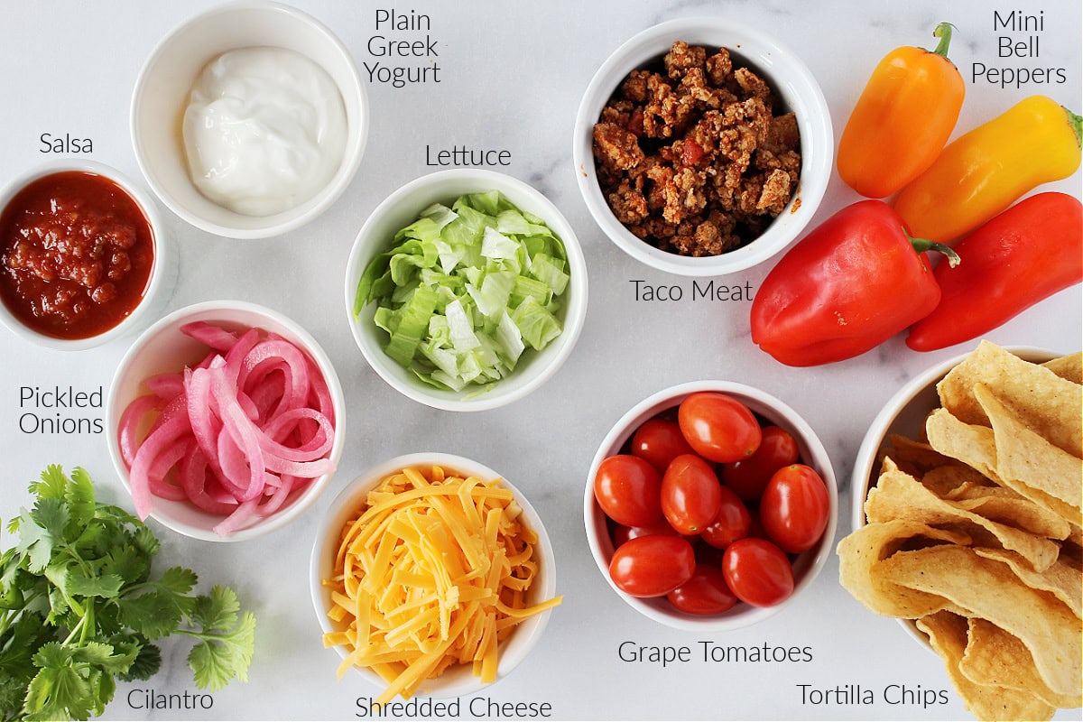 Labeled ingredients for healthy nachos on a white marble countertop.