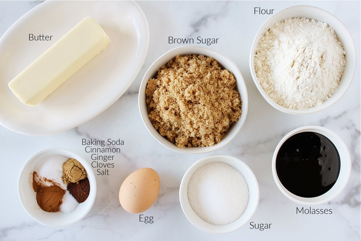 Labeled ingredients for molasses crinkle cookies on a white marble countertop.