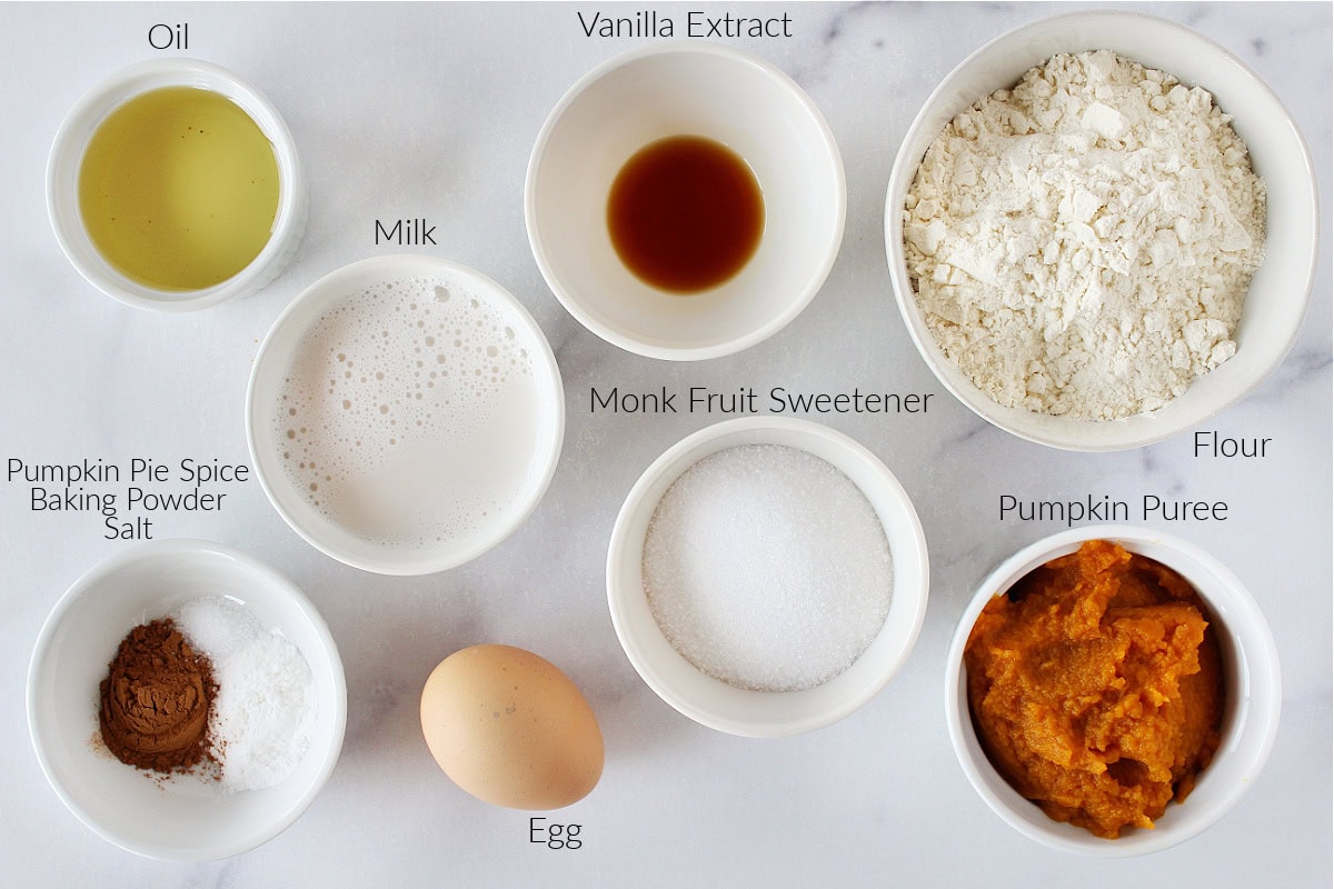 Labeled ingredients for baked pumpkin donuts on a white marble countertop.