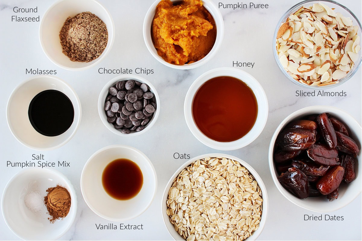 Labeled ingredients for no bake chocolate chip pumpkin energy balls on a white marble countertop.