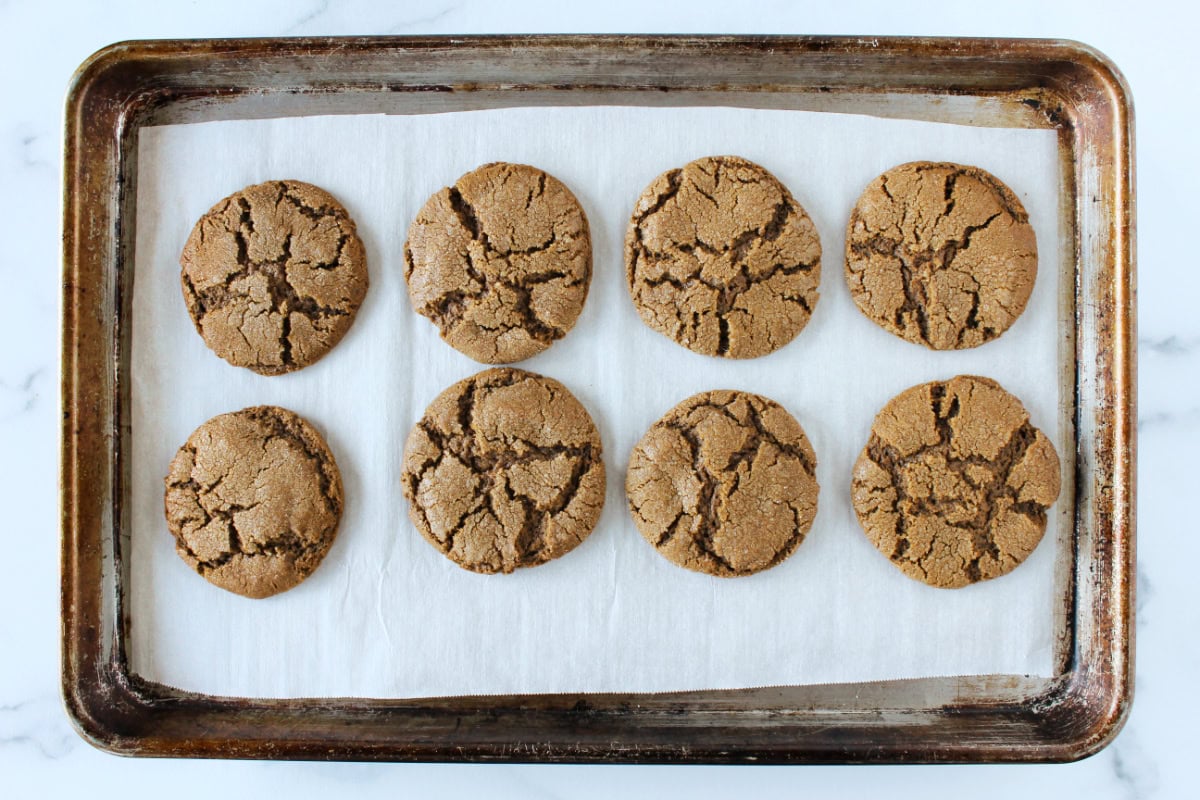 Eight crinkled molasses cookies on a baking sheet.