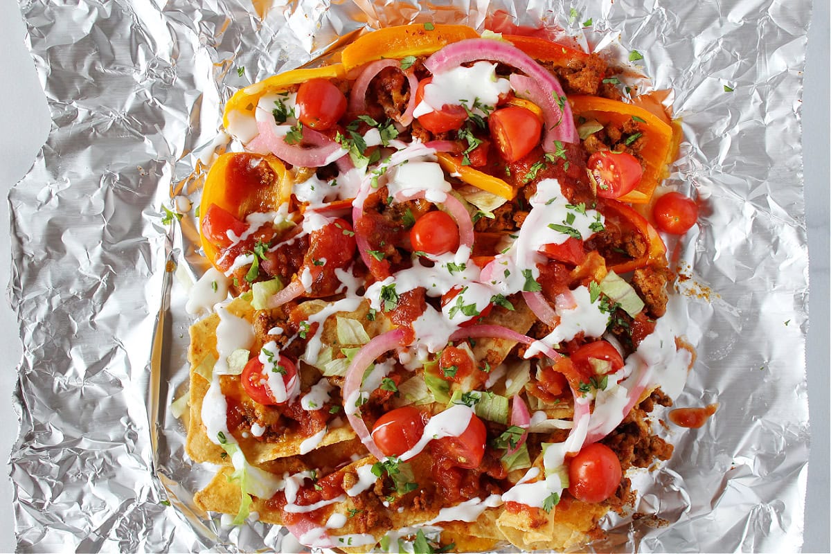Pickled onions, tomatoes, and cilantro on nachos on a piece of aluminum foil.