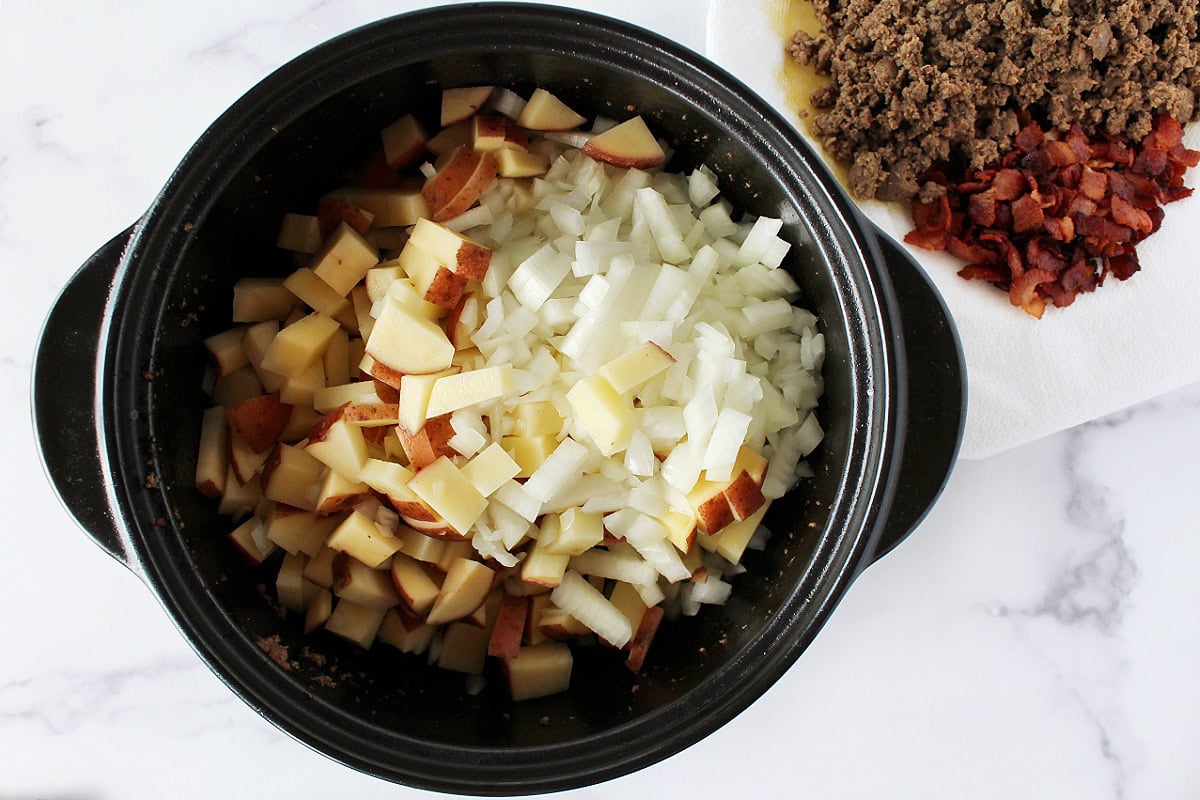 Potatoes and onion in a pot with browned turkey sausage and bacon on the side.