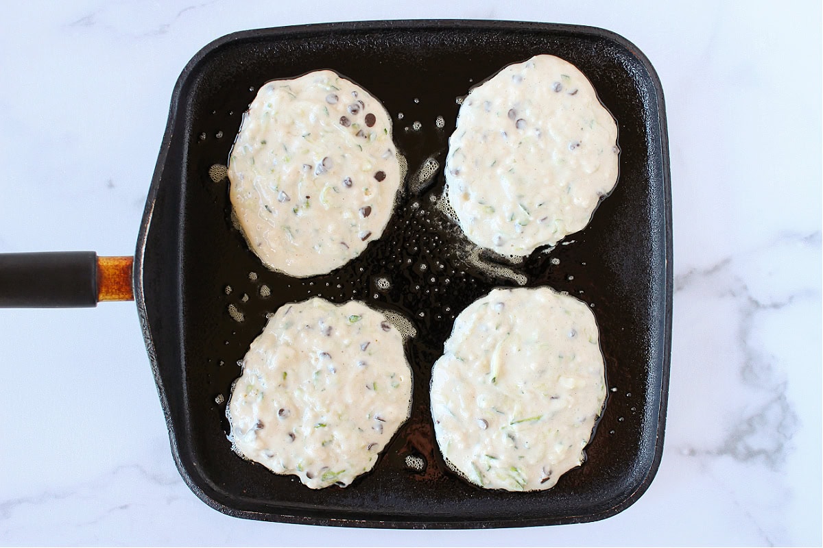 Zucchini pancake batter with chocolate chips on a black griddle.