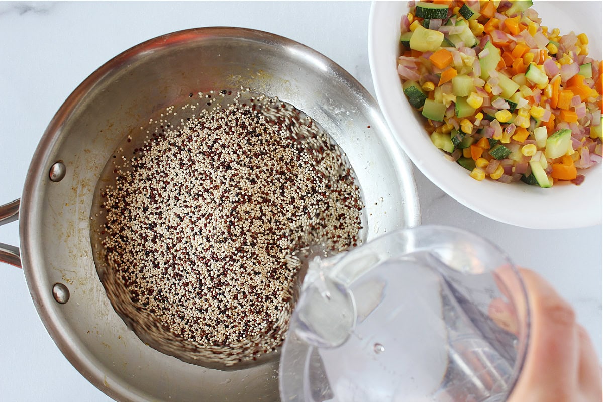Pouring water into a sauté pan with uncooked quinoa.