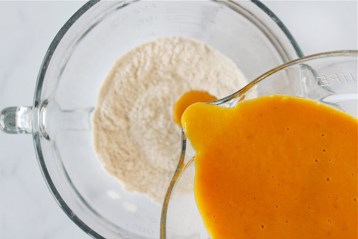 Pouring the wet batter into the dry ingredients for pumpkin donuts.