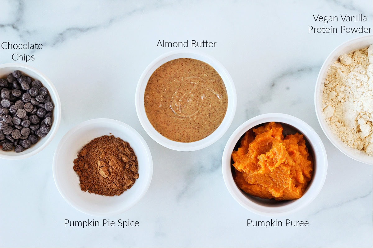 Labeled ingredients for no bake pumpkin protein balls on a white marble countertop.