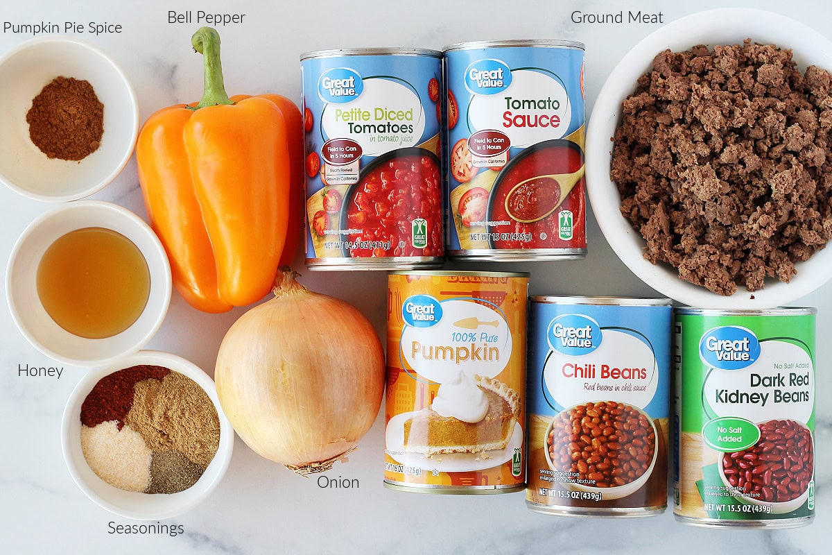 Labeled ingredients for pumpkin chili on a white marble countertop.