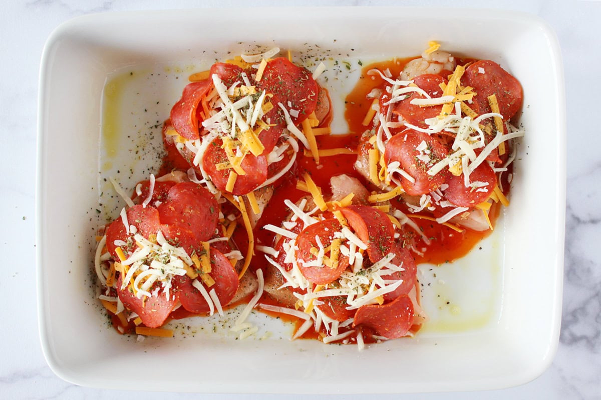Four chicken breasts in a pan topped with turkey pepperoni, cheese and pizza sauce.