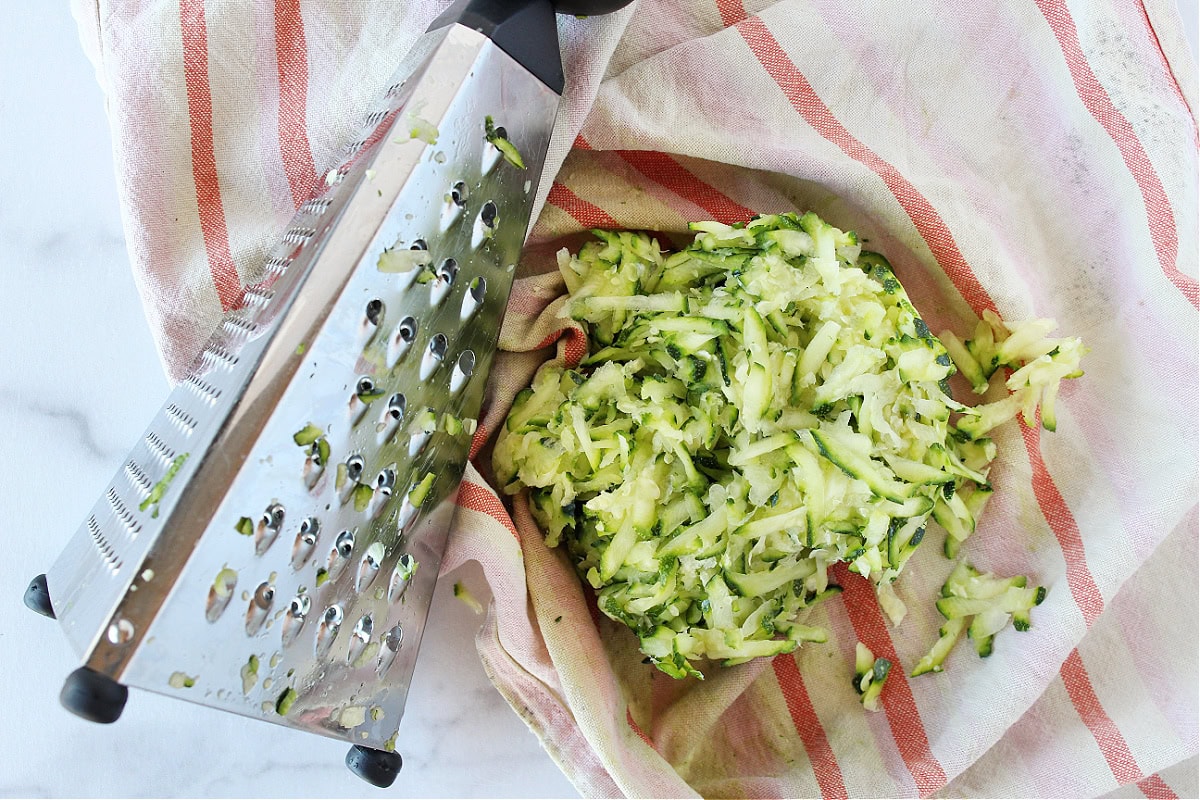 Shredded zucchini on a towel with the box grater.