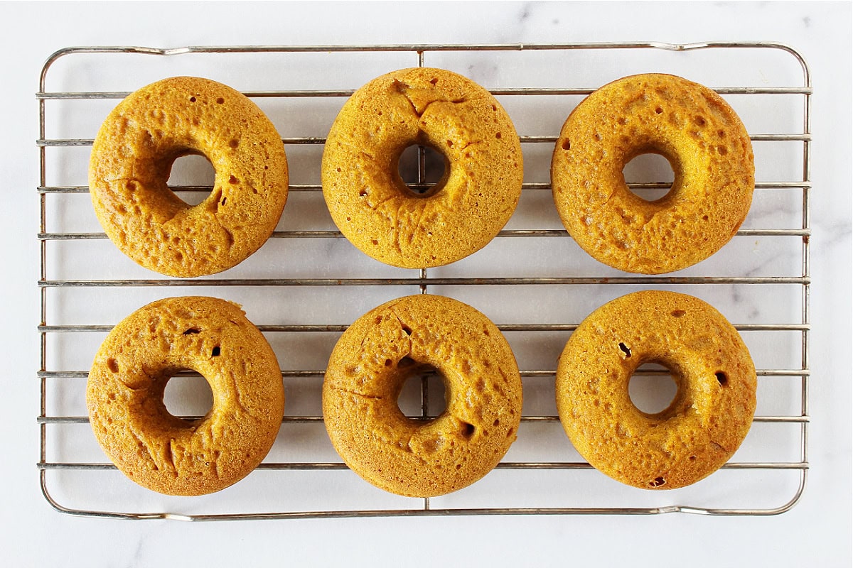 Six pumpkin donuts on a metal cooling rack.