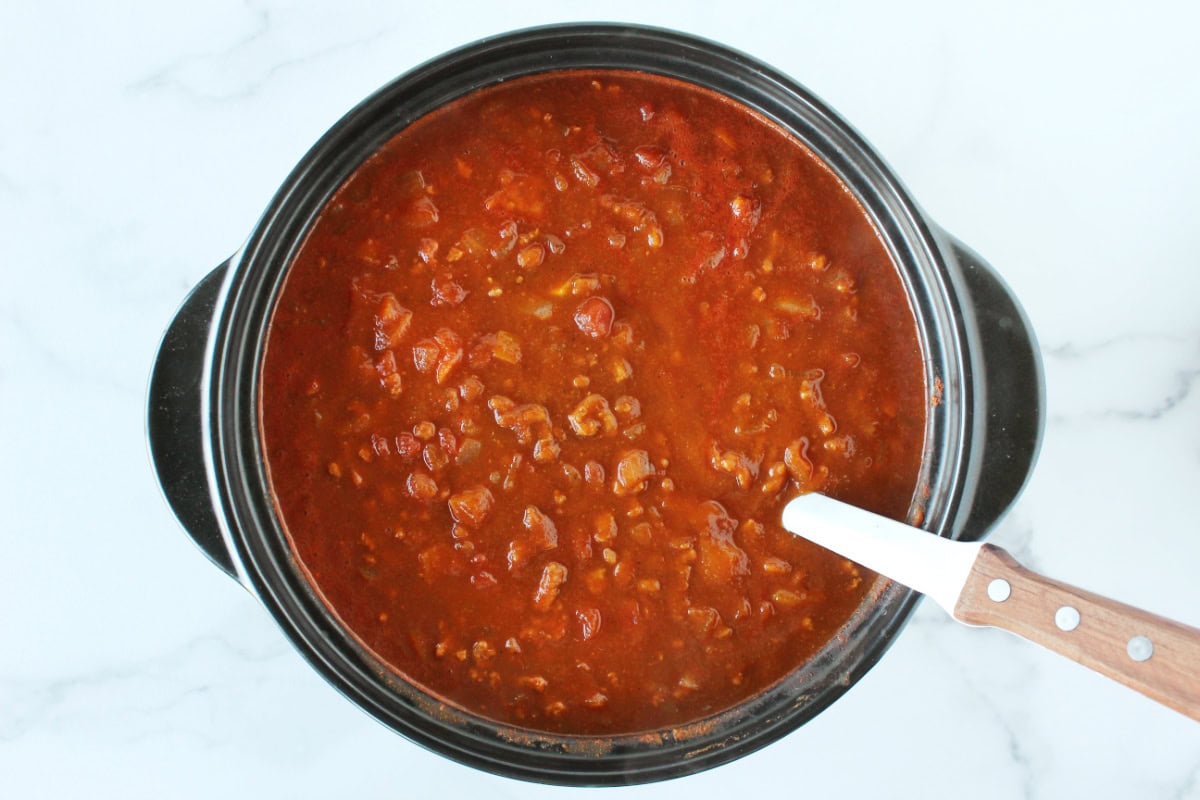 Thick chili in a black soup pot with a ladle.