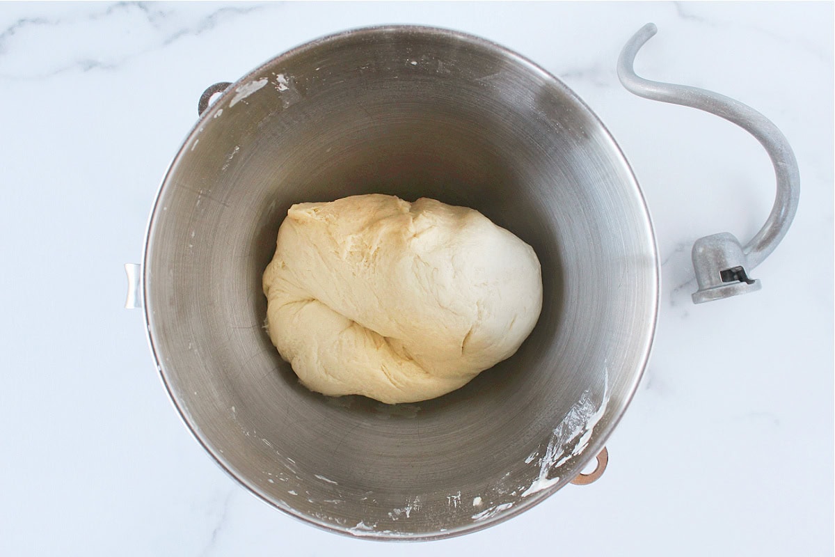 Bread dough in a metal stand mixer bowl with the dough hook.