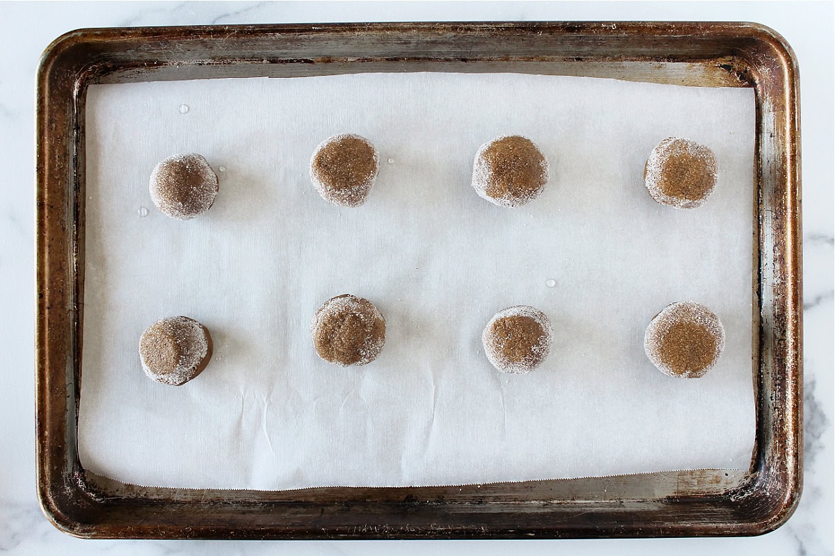 Eight molasses crinkle dough balls coated in sugar and sprinkled with a drop of water.