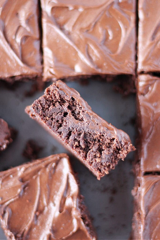 A frosted brownie on it's side in the pan of brownies.