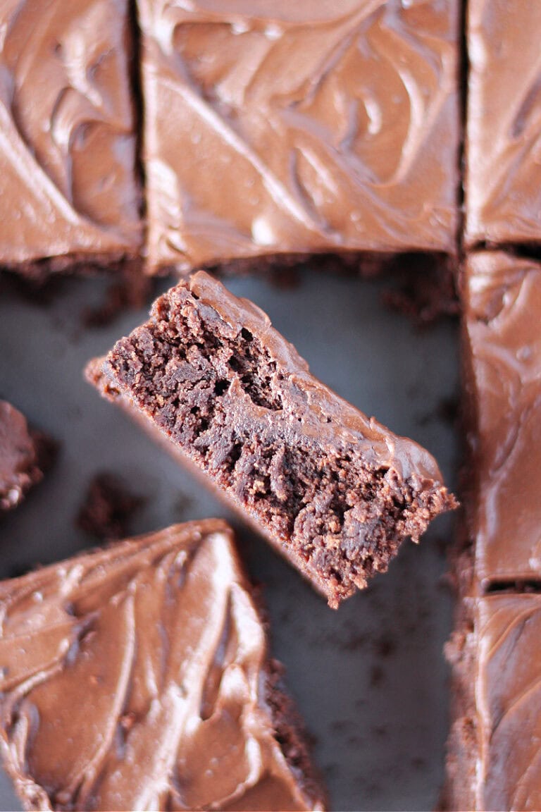 A frosted brownie on it's side in the pan of brownies.