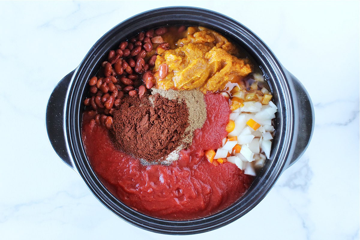 Pumpkin puree, tomato sauce, chili beans and diced onion in a black pot.