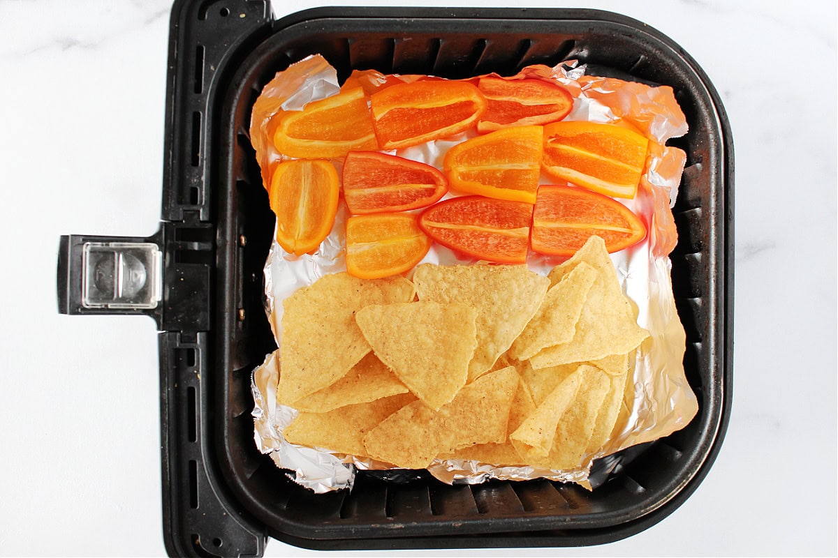 Mini bell pepper halves and tortilla chips in an air fryer for nachos.
