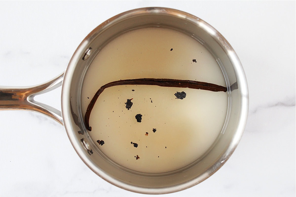 Vanilla bean in sugar and water in a small metal pot.