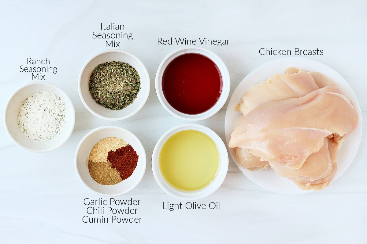 Labeled ingredients for zesty crockpot chicken on a white marble countertop.