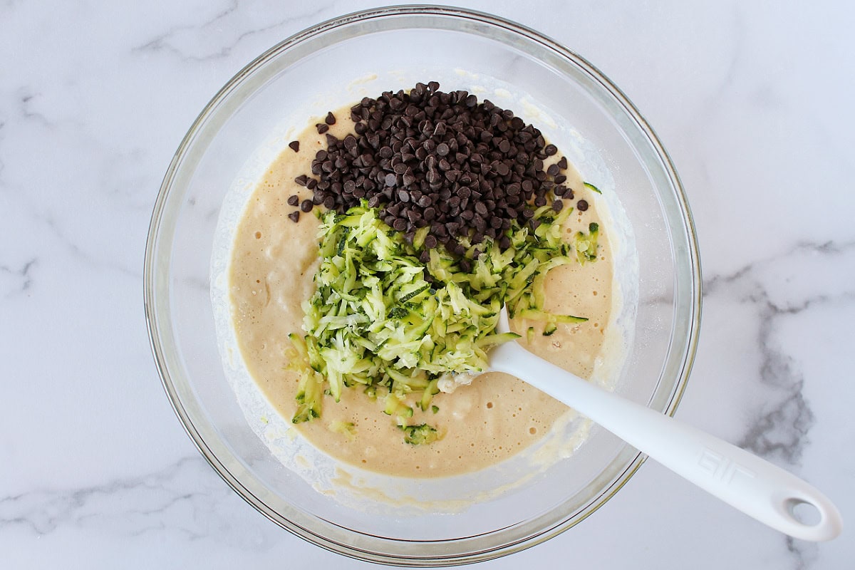 Shredded zucchini and mini chocolate chips on top of pancake batter in a bowl.