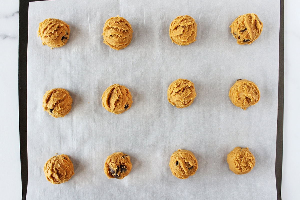 Twelve cookie dough balls on a baking sheet lined with parchment paper.