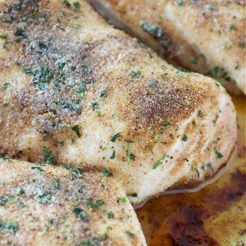 Seasoned baked chicken breasts in pan juices.