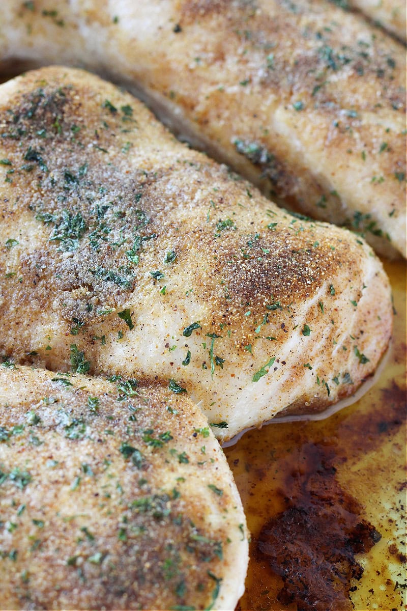 Seasoned baked chicken breasts in pan juices.