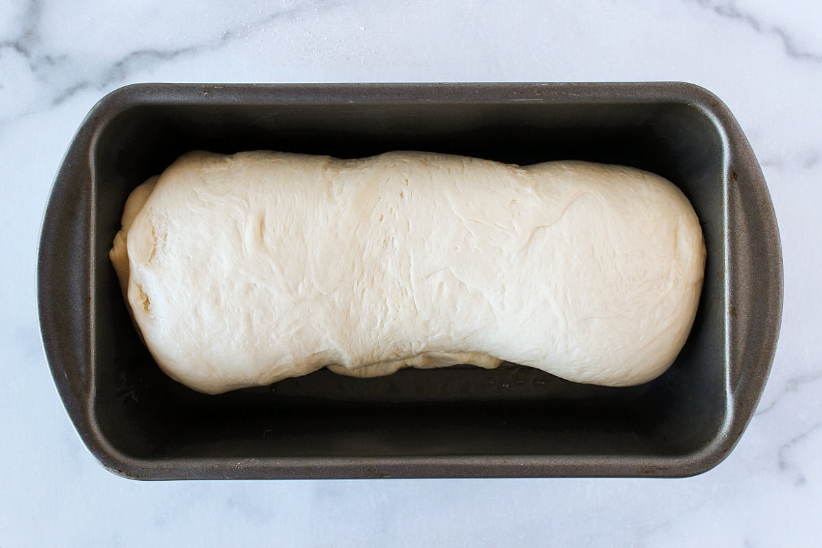 Rolled up sourdough bread log in a metal pan.